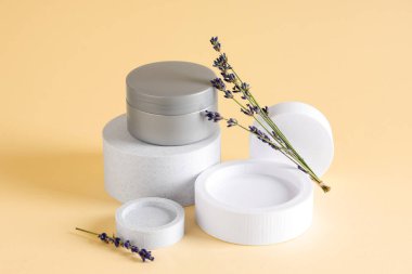 Sarı arka planda kozmetik krem kavanozu ve lavanta çiçekleriyle dekoratif podyumlar