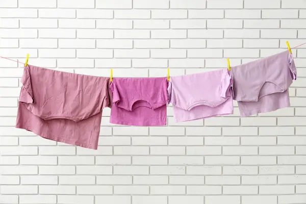 stock image Clean t-shirts hanging on rope against light brick wall