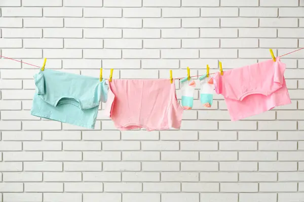 stock image Clean clothes hanging on rope against light brick wall