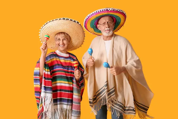 stock image Mature couple in sombrero hats with Mexican maracas on yellow background