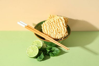 Çiğ erişte, fesleğen, kireç ve renkli arka planda ahşap çubuklarla dolu bir kâse.