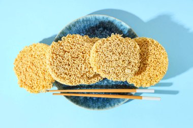 Çiğ erişte tabağı ve mavi arka planda ahşap yemek çubukları.