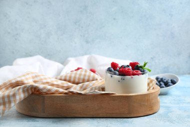Farklı taze böğürtlenli ve açık mavi arkaplanda naneli bir bardak lezzetli yoğurt.