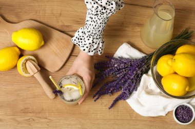 Ahşap masada taze lavantalı limonata ve meyve sıkacağı olan bir kadın eli.
