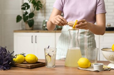 Mutfaktaki masada lavantalı limonata hazırlamak için limon sıkan genç kadın.