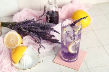 Bir bardak taze lavantalı limonata, çiçekler ve beyaz fayanslı meyve sıkacağı.
