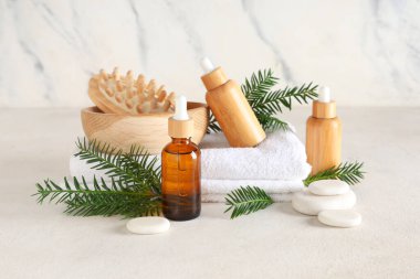 Temel yağ şişeleri, spa aksesuarları ve hafif arkaplanda köknar dalları olan kompozisyon