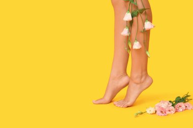 Sarı arka planda güzel Eustoma çiçekleri olan genç bir kadının bacakları.