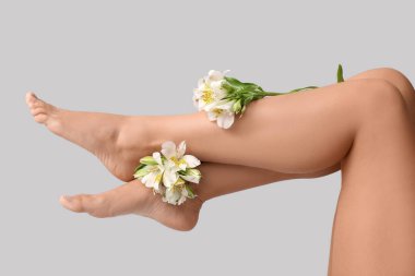 Gri arka planda güzel alstromerya çiçekleri olan genç bir kadının bacakları