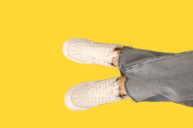 Sarı arka planda şık beyaz ayakkabılı genç kadın bacakları.