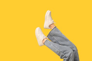 Sarı arka planda şık beyaz ayakkabılı genç kadın bacakları.