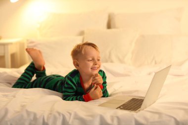 Geceleri yatak odasında dizüstü bilgisayarda çizgi film izleyen şirin bir çocuk.