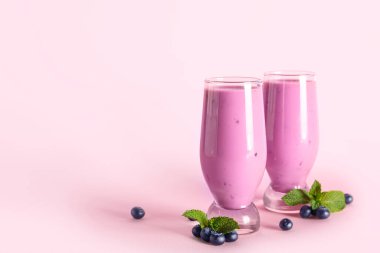 Bir bardak taze böğürtlenli, naneli ve pembe arkaplanlı meyve püresi.