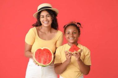 Güzel, genç, Afro-Amerikan kadın ve tatlı kızı kırmızı arka planda taze karpuz kesiyorlar.