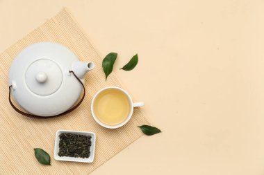 Bej arka planda kurumuş yapraklı çay fincanı ve çaydanlık.