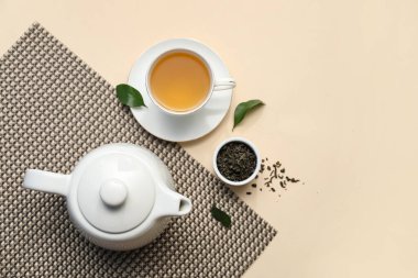 Bej arka planda kurumuş yapraklı çay fincanı ve çaydanlık.