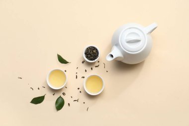 Bej arka planda kurumuş yapraklı sıcak çay kaseleri ve çaydanlık.