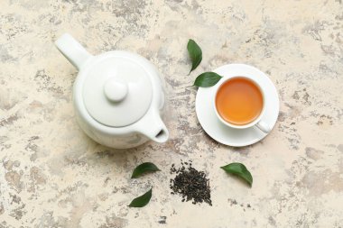 Arkaplanda kurumuş yapraklı çay fincanı ve çaydanlık.