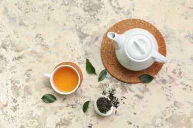 Arkaplanda kurumuş yapraklı çay fincanı ve çaydanlık.