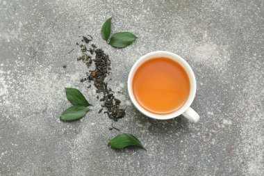 Bir fincan sıcak çay ve gri arka planda kurumuş yapraklar.