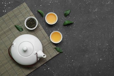 Siyah arka planda kurumuş yapraklı sıcak çay kaseleri ve çaydanlık.