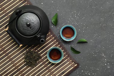 Siyah arka planda kurumuş yapraklı sıcak çay kaseleri ve çaydanlık.