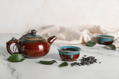 Beyaz arka planda kurumuş yapraklı sıcak çay kaseleri ve çaydanlık.