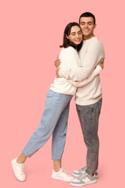 Pembe arka planda kucaklaşan neşeli genç çift