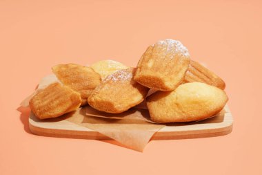 Lezzetli madeleine ve turuncu arka planda pudra şekerli ahşap tahta.