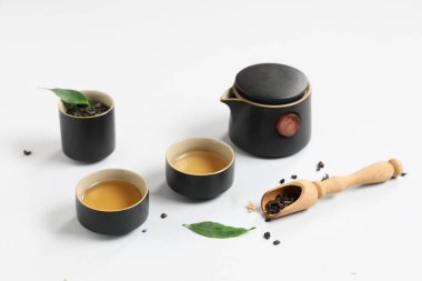 Bardaklı çaydanlık, bir kepçe kuru çay ve beyaz arka planda yapraklar.