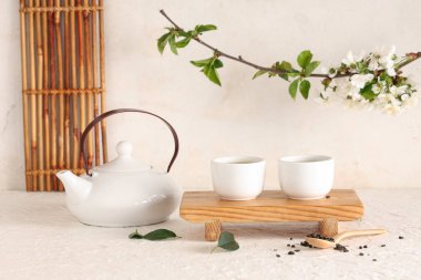 Çaydanlık, fincanlar, bir kaşık kuru çay ve arka planda yapraklar olan ahşap tezgah.