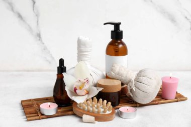 Farklı kozmetik ürünleri olan spa malzemeleri, bitki torbaları, masaj fırçası ve beyaz arka planda yanan mumlar.