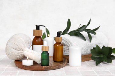 Farklı kozmetik ürünleri içeren spa malzemeleri, bitkisel çanta, havlu ve bej fayans masasında yanan mumlar.
