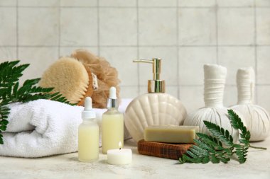 Beyaz masa üzerinde kozmetik yağ şişeleri, bitkisel torbalar ve eğrelti otu dalları ile spa malzemeleri seti