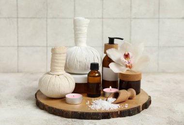 Farklı kozmetik ürünleri içeren spa malzemeleri, deniz tuzu, bitkisel torbalar ve beyaz masada yanan mumlar.