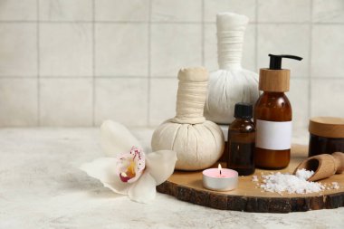 Farklı kozmetik ürünleri içeren spa malzemeleri, deniz tuzu, bitkisel torbalar ve beyaz masada yanan mum.