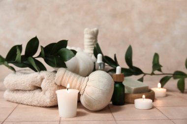 Kozmetik yağlı spa malzemeleri, bitkisel poşetler, banyo süngeri, sabun barı ve bej döşeme masasında yanan mumlar.