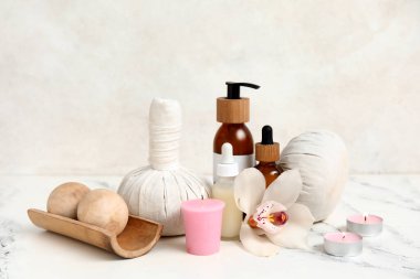 Farklı kozmetik ürünleri, bitkisel poşetler, orkide çiçeği ve beyaz arka planda yanan mumlar içeren spa malzemeleri.