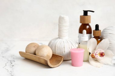 Farklı kozmetik ürünleri, bitkisel poşetler, orkide çiçeği ve beyaz arka planda yanan mumlar içeren spa malzemeleri.