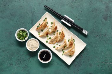 Kızarmış Japon gyoza tabağı, yeşil soğan ve arka planda bir kase soya sosu.