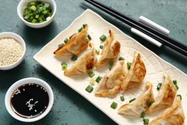 Kızarmış Japon gyoza tabağı, yeşil soğan ve arka planda bir kase soya sosu.