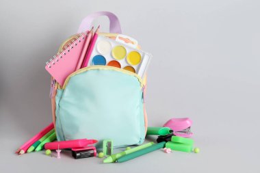 Gri arka planda okul malzemelerinin olduğu sırt çantası.