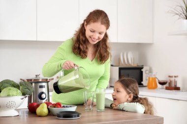 Anne ve küçük kızı mutfaktaki bardaklara smoothie dolduruyorlar.