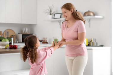 Anne, küçük kızına mutfakta bir bardak sağlıklı meyve suyu veriyor.