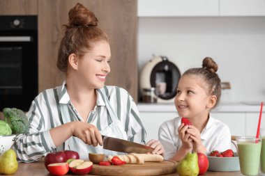 Anne ve küçük kızı mutfakta meyve suyu için meyve doğruyor.