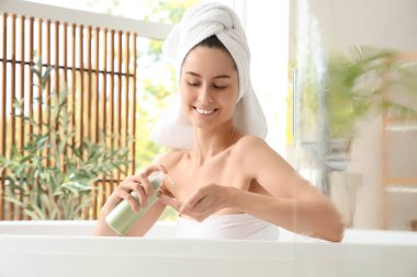 Bir şişe şampuanla evde banyo yapan güzel, genç ve mutlu bir kadın.