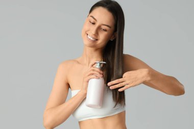 Gri arka planda bir şişe şampuanı olan güzel, mutlu genç bir kadın.