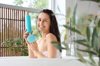 Saçına masaj yapan, banyoda şampuan şişesi olan güzel, genç ve mutlu bir kadın.