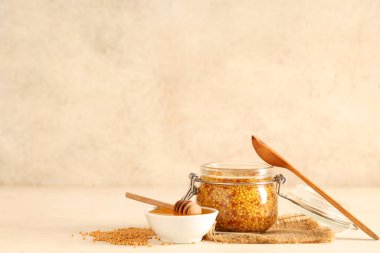 Dijon hardallı kavanoz ve bej arka planda bir kase bal.