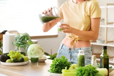Farklı sebzelerle genç ve güzel bir kadın mutfaktaki cama sağlıklı yeşil meyve püresi döküyor. Diyet kavramı
